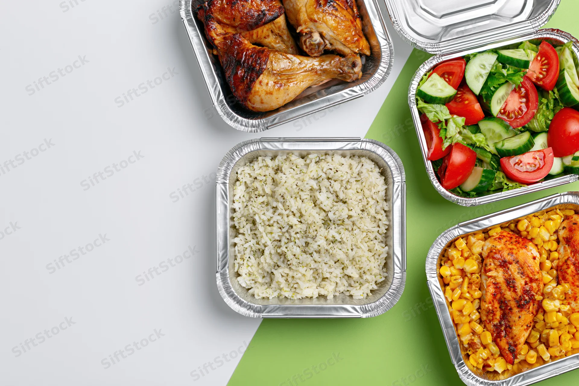 Four aluminum foil takeout containers with chicken, rice, salad and corn arranged on white and green surface