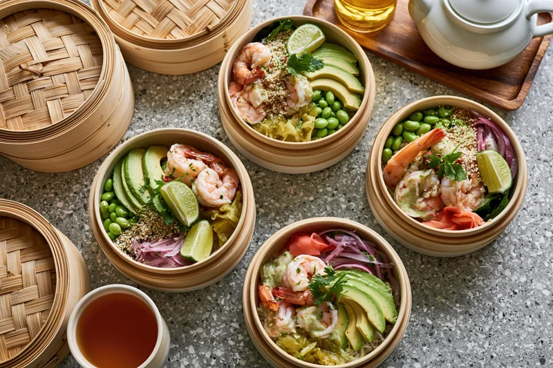 Four poke bowls with shrimp, avocado, edamame and lime in bamboo steamers on a terrazzo countertop with tea cups nearby