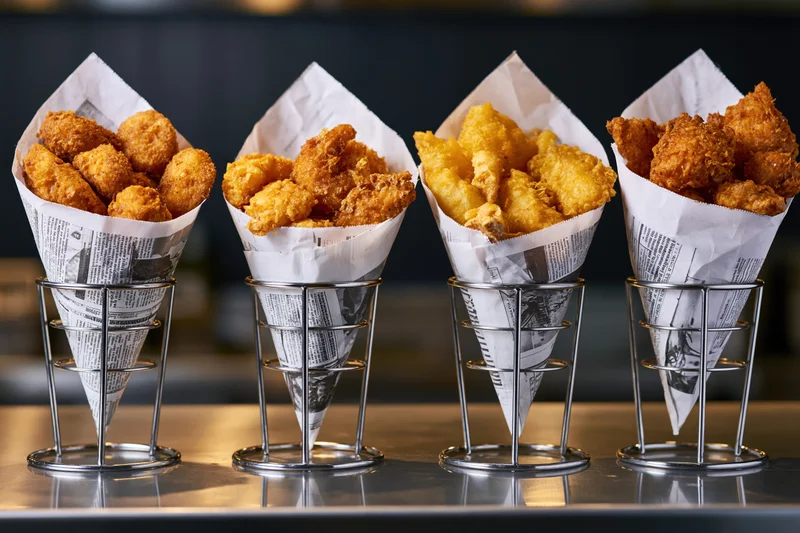 Four metal cone holders each filled with fried chicken pieces lined up on a reflective restaurant counter
