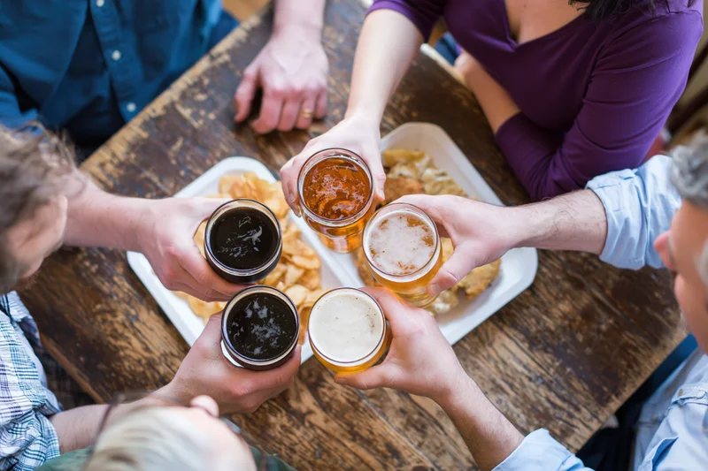 Friends raising beer glasses in toast around wooden pub table