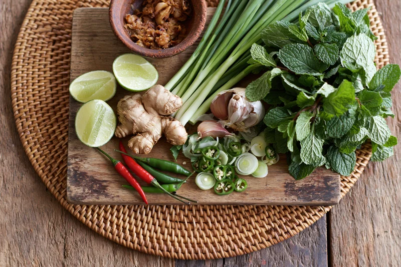 Fresh vietnamese pho ingredients arranged on a wooden cutting board with mint, lime, ginger, garlic, chilies and green onions