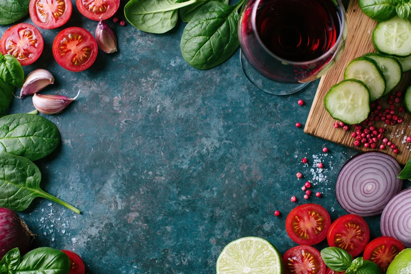Fresh salad ingredients arranged around edges of dark stone surface with copyspace in center