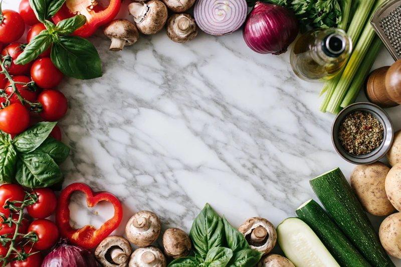 Fresh vegetables and herbs arranged in a border frame on a marble countertop
