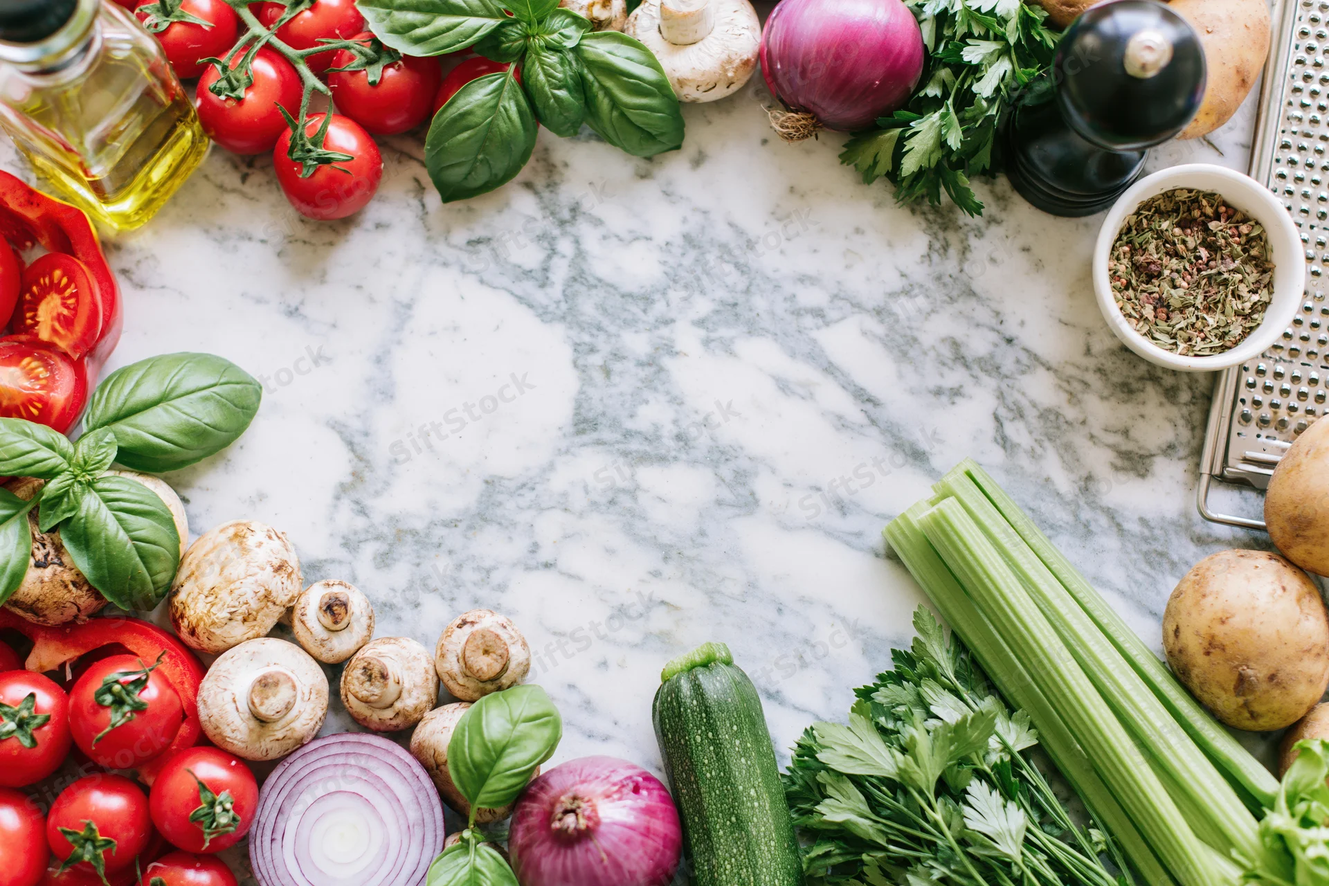 Fresh vegetables and herbs arranged in a border frame around a marble countertop