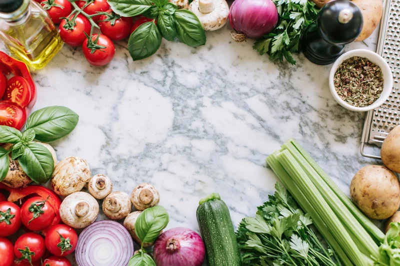 Fresh vegetables and herbs arranged in a border frame around a marble countertop