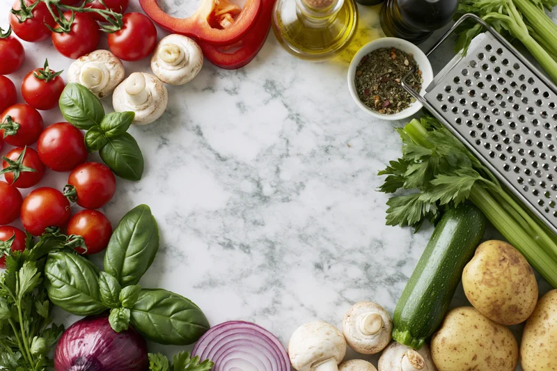 Fresh vegetables and herbs arranged in a border frame on a marble countertop