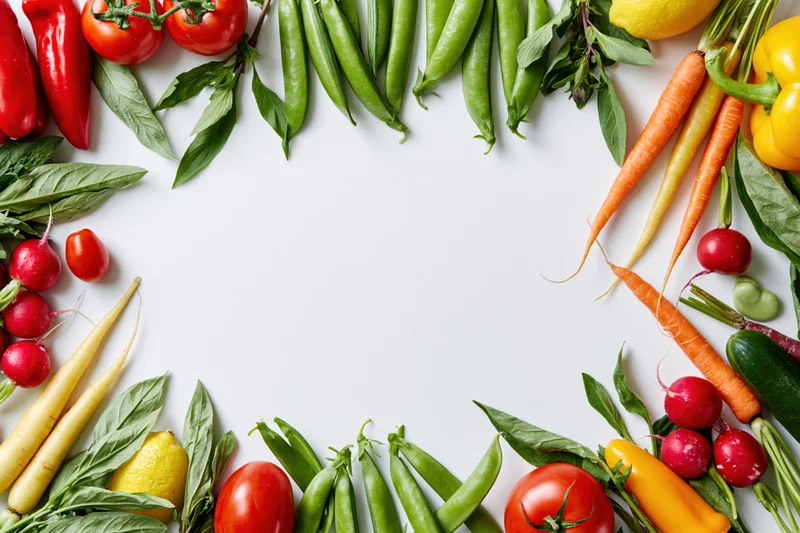 Fresh vegetables and herbs arranged in a flat lay border frame on white background with copyspace