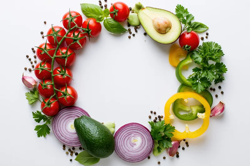 Fresh vegetables and herbs arranged in a loose circular border on white background with copyspace
