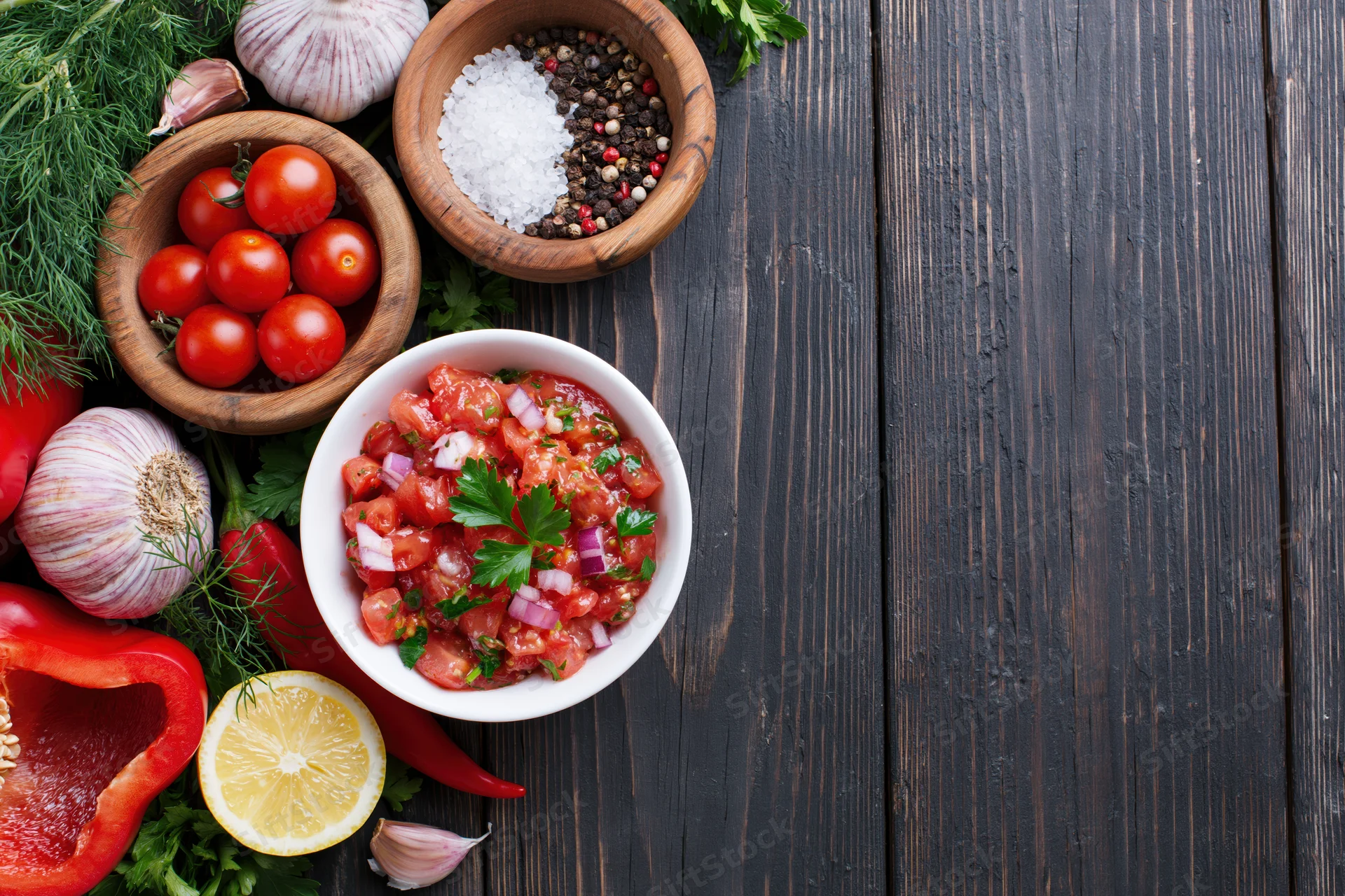 Salsa in a white bowl surrounded by fresh vegetables and herbs on a dark wooden table