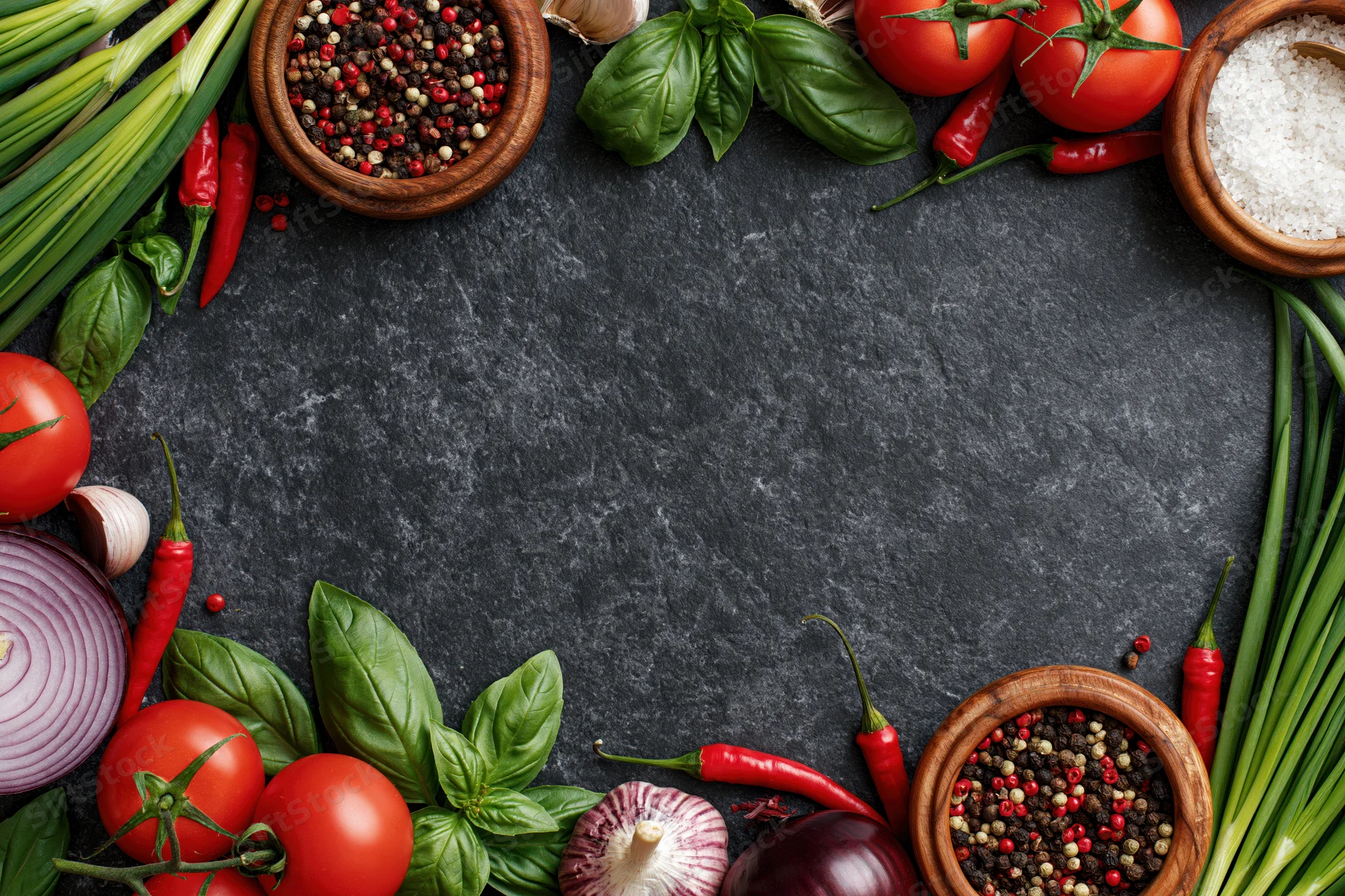 Fresh vegetables and spices arranged in a border frame around a dark surface with copyspace in center