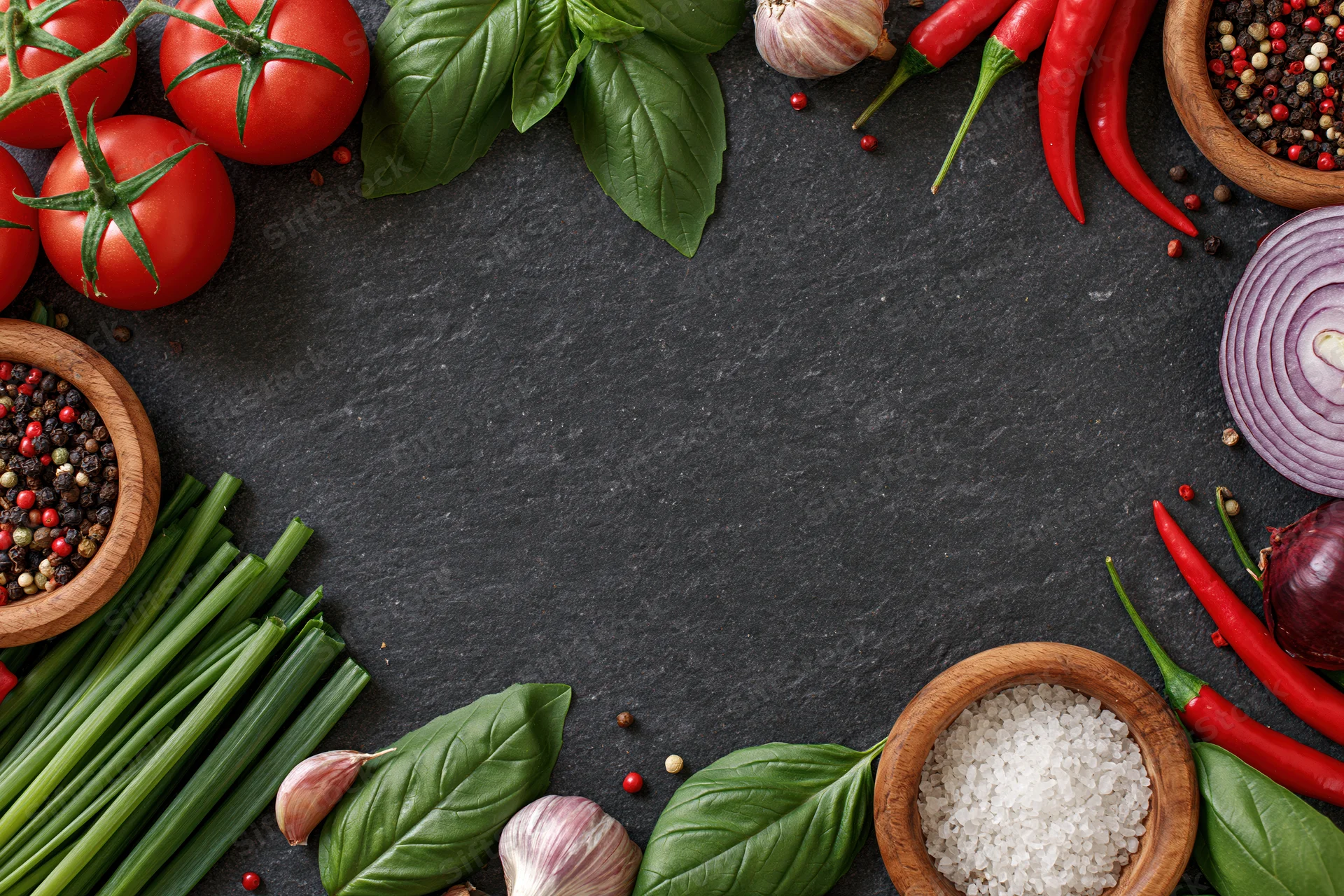Fresh vegetables and spices arranged in a border frame on a dark slate surface