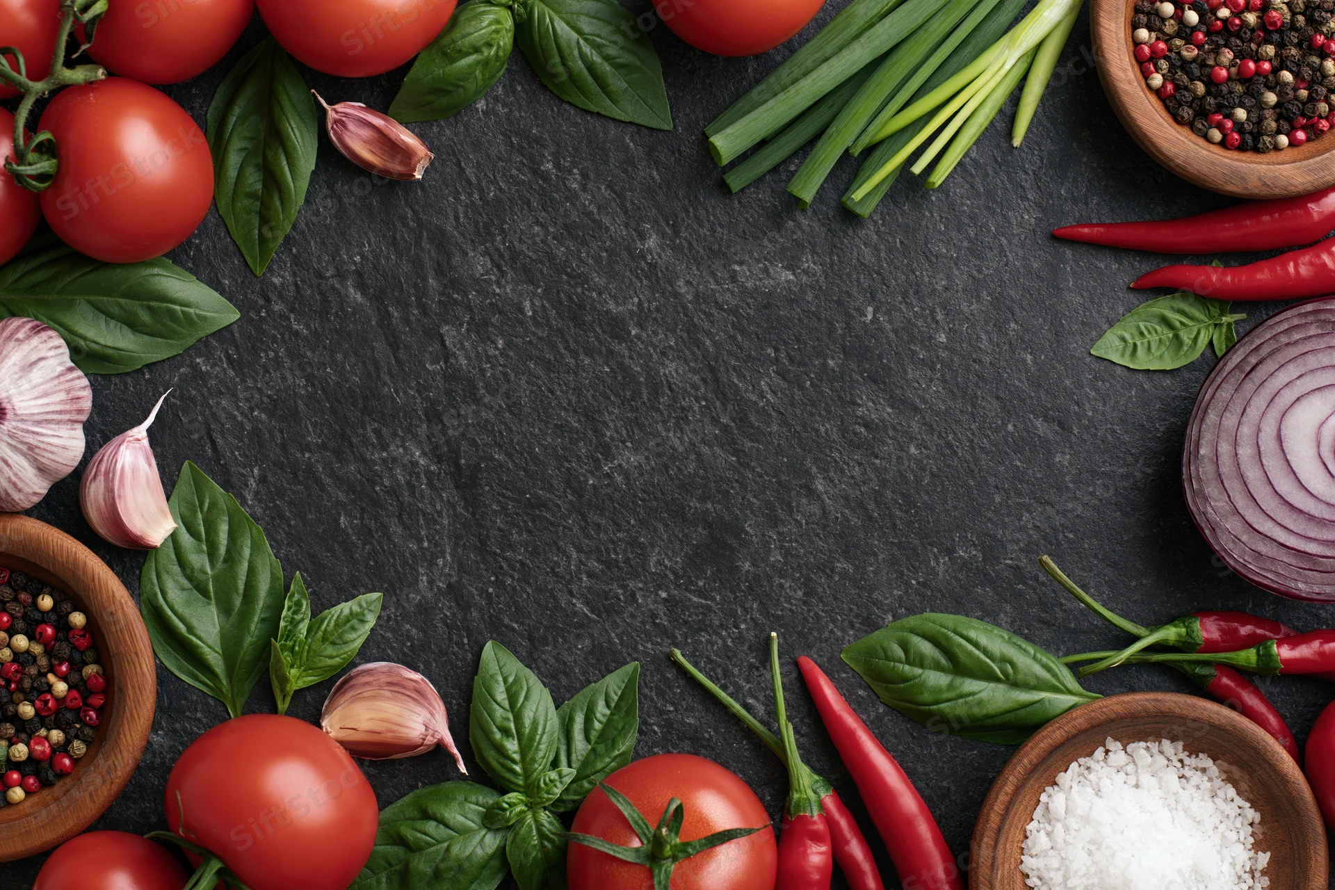 Fresh vegetables and spices arranged in a border frame on dark slate surface with central copyspace