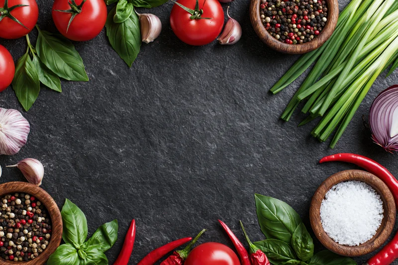 Fresh vegetables and spices arranged in a border frame on a dark slate surface