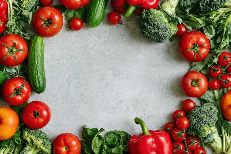 Fresh vegetables arranged in a border frame around a central copyspace on a countertop