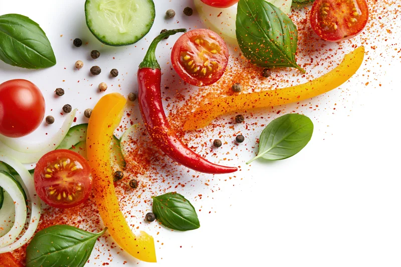 Fresh vegetables and herbs arranged with spices on white surface