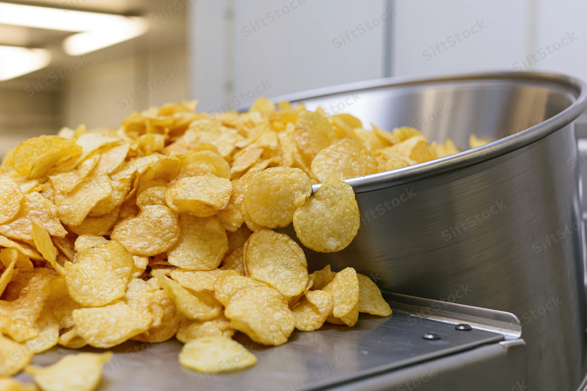 Freshly made potato chips tumbling out of a stainless steel container in a factory setting