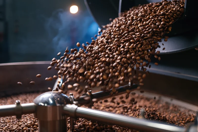 Roasted coffee beans cascading from industrial roasting machine in factory setting
