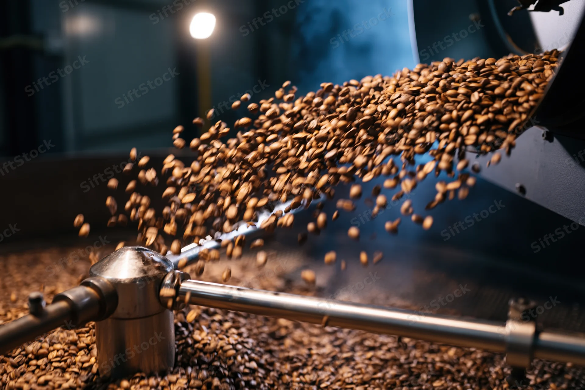 Roasted coffee beans cascading from industrial roasting machine in factory interior