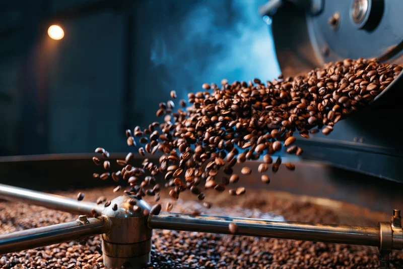 Roasted coffee beans cascading from industrial roasting machine in dim factory interior