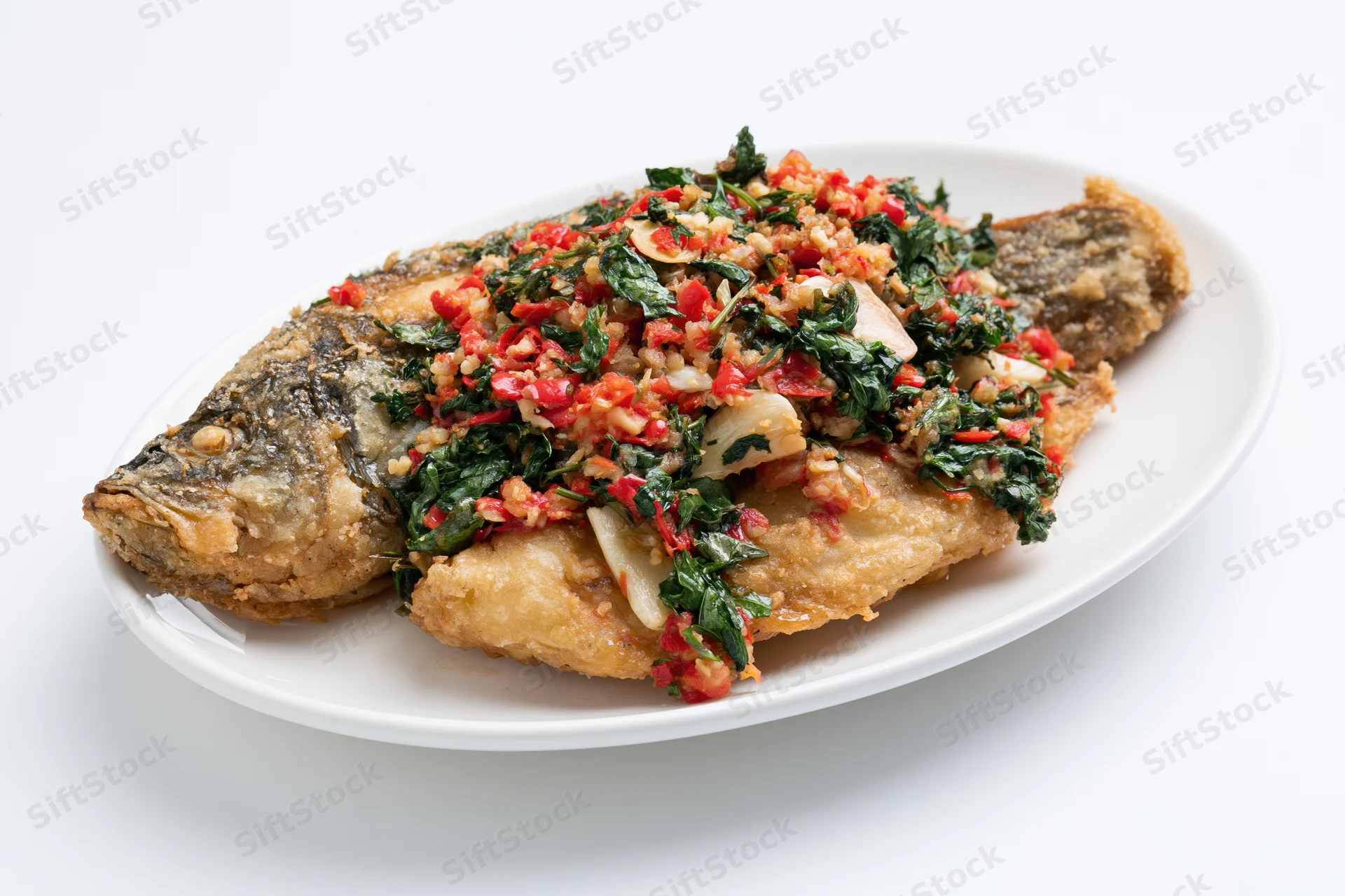 Whole fried fish topped with stir-fried thai basil and chili on a white plate