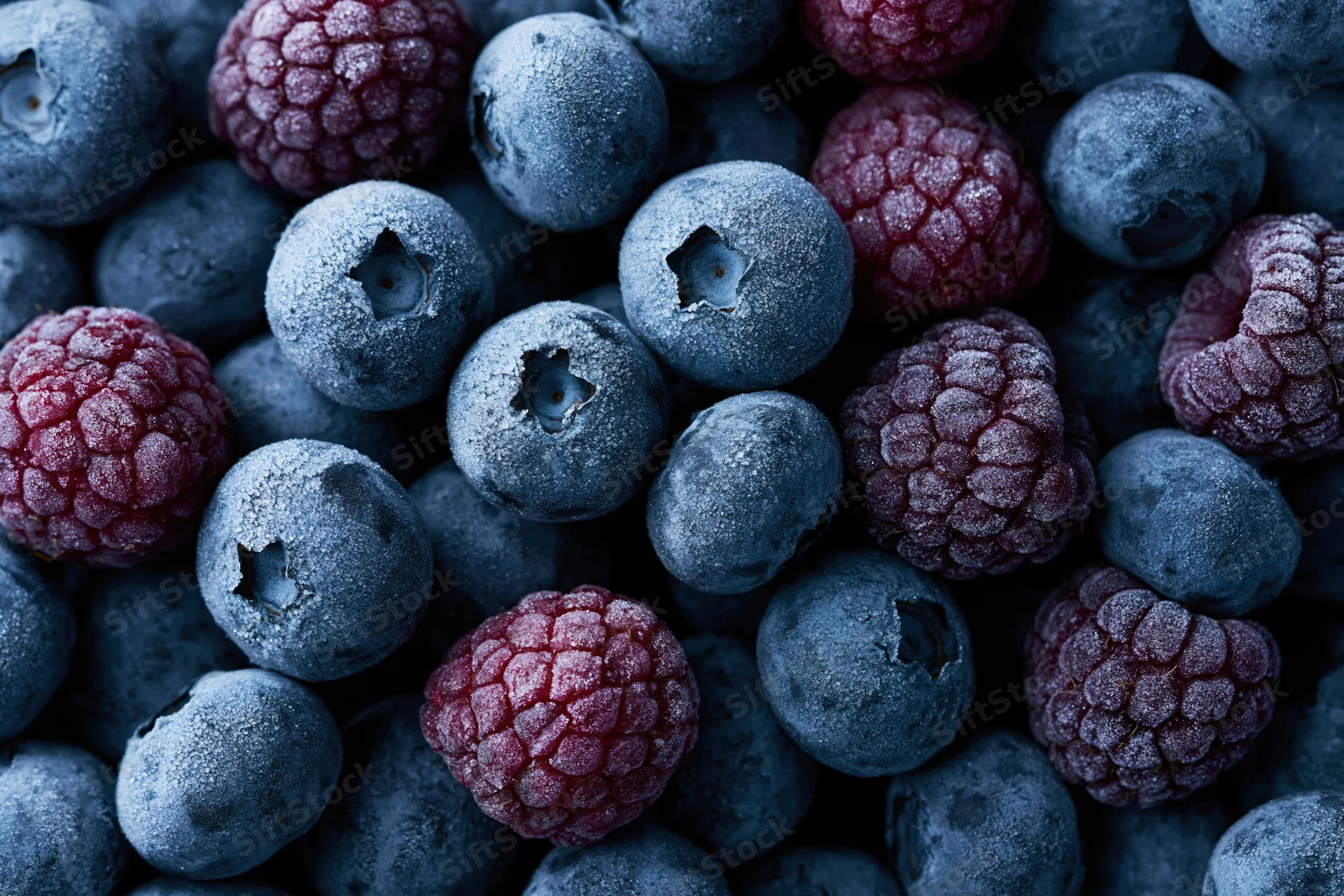 Frozen blueberries and raspberries tightly packed in a close-up view