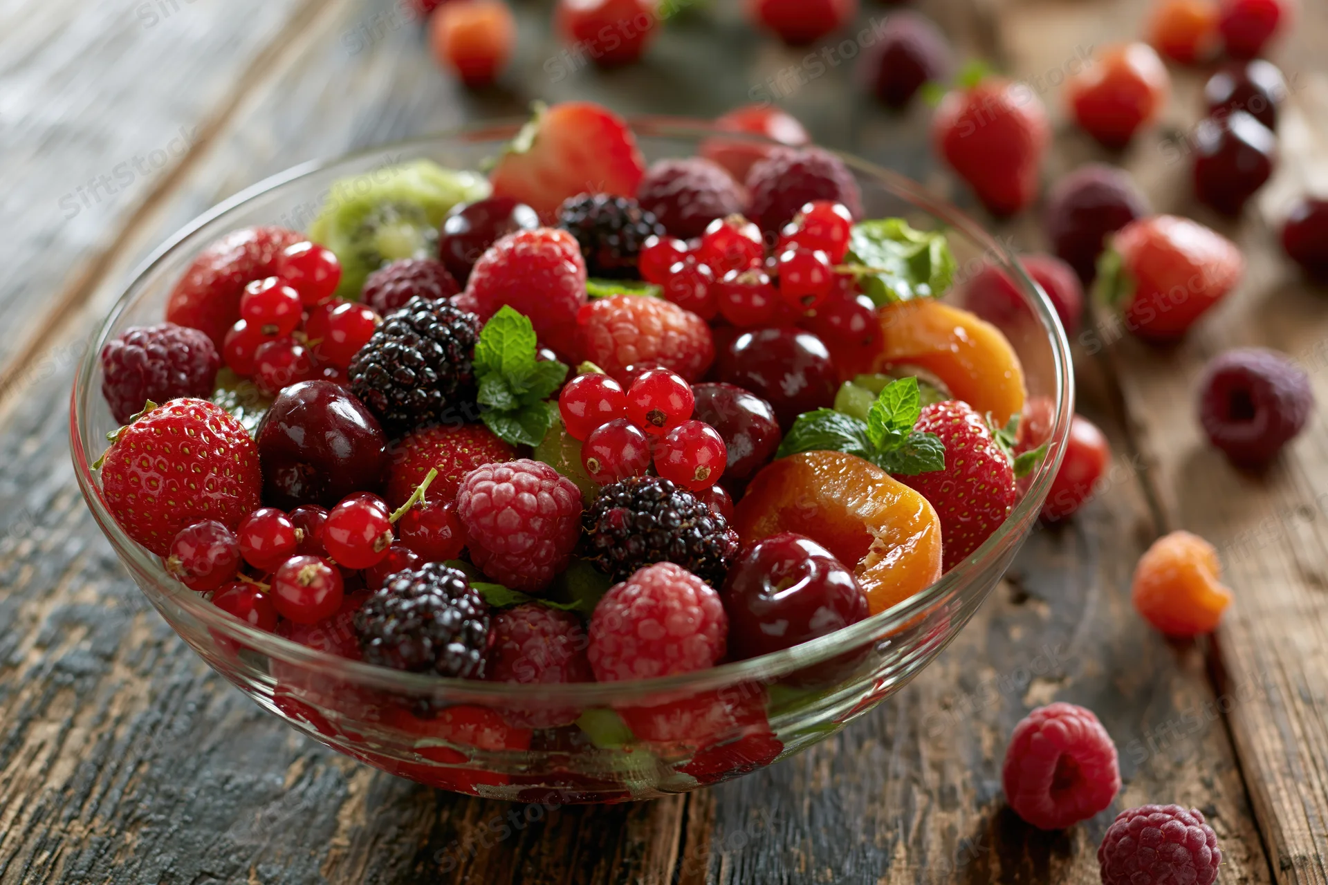 Glass bowl filled with mixed fresh berries and fruit on a rustic wooden table