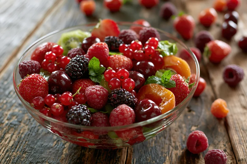 Glass bowl filled with mixed fresh berries and fruit on a rustic wooden table