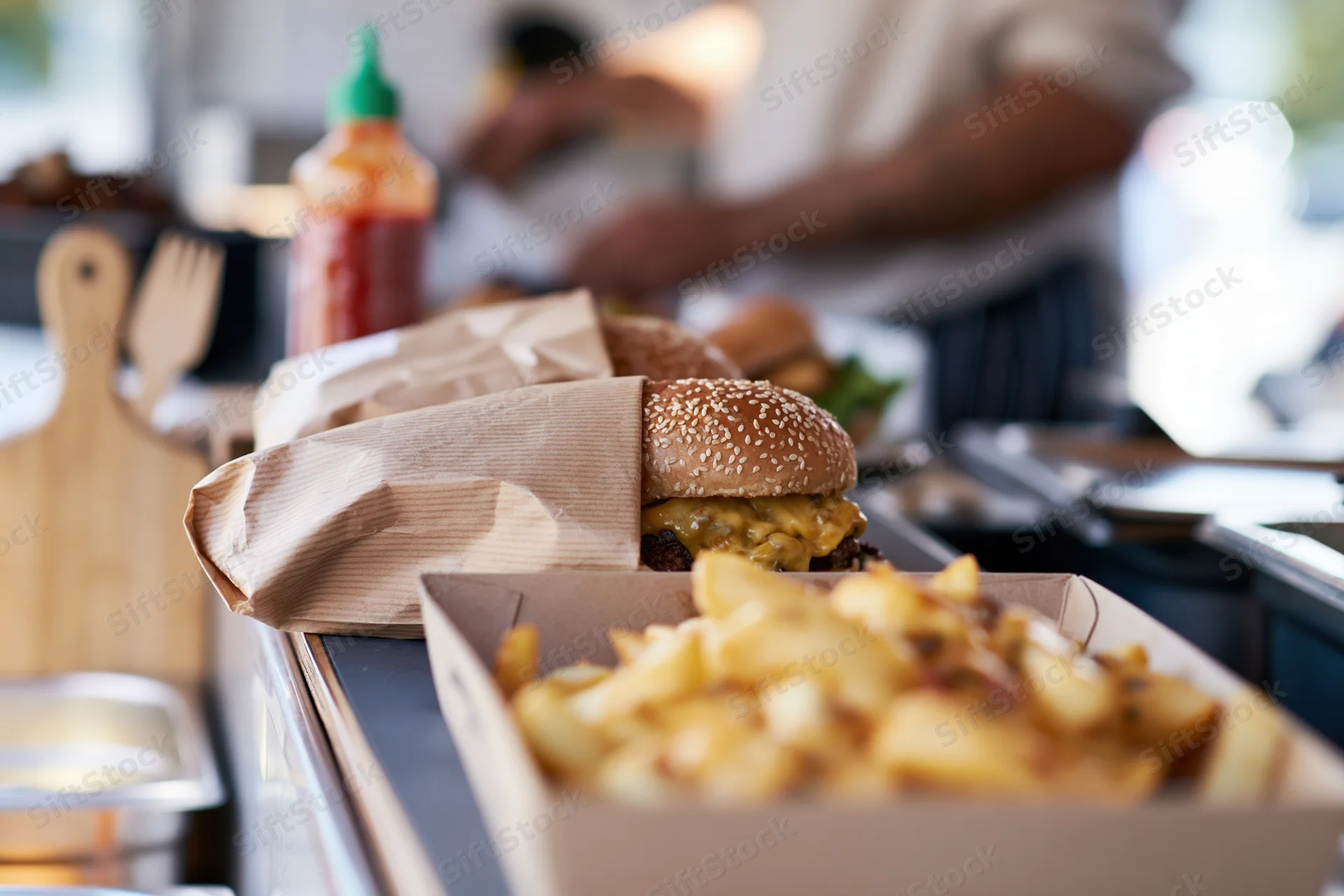 Cheeseburger wrapped in kraft paper with fries in a cardboard box on a kitchen counter