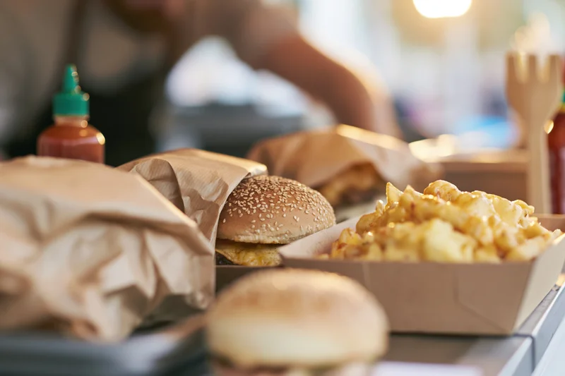 Gourmet burgers wrapped in kraft paper with cheese fries on a tray in a casual dining setting