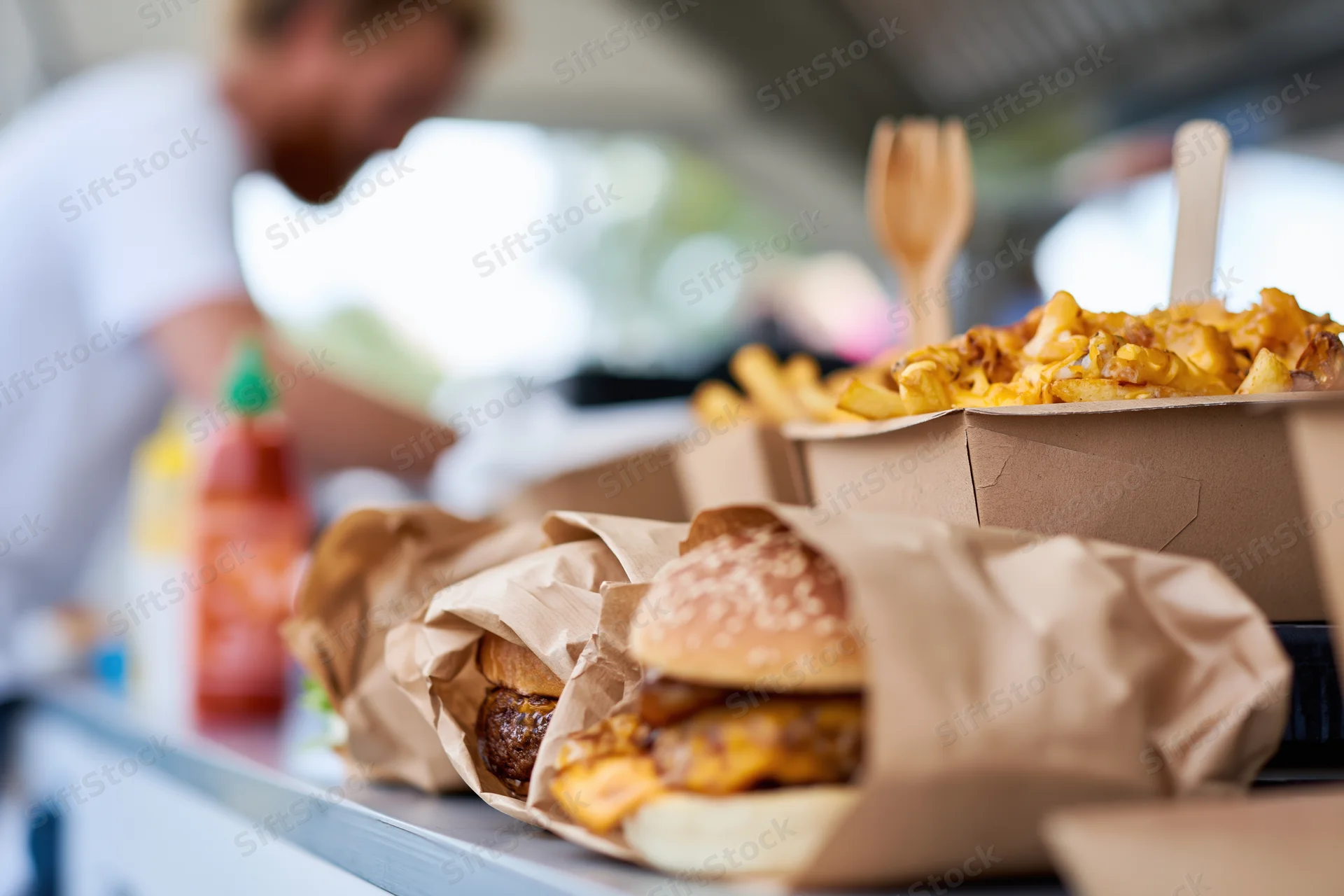 Gourmet burgers wrapped in kraft paper and cheese fries on a food truck counter