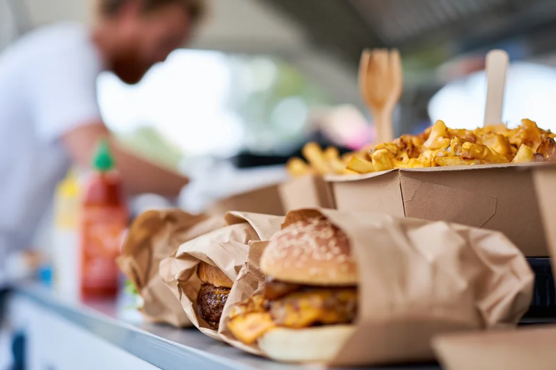 Gourmet burgers wrapped in kraft paper and cheese fries on a food truck counter