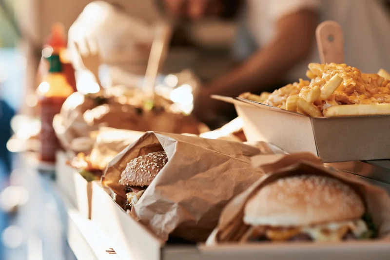 Gourmet burgers wrapped in kraft paper and cheese fries served on a tray at an outdoor dining table