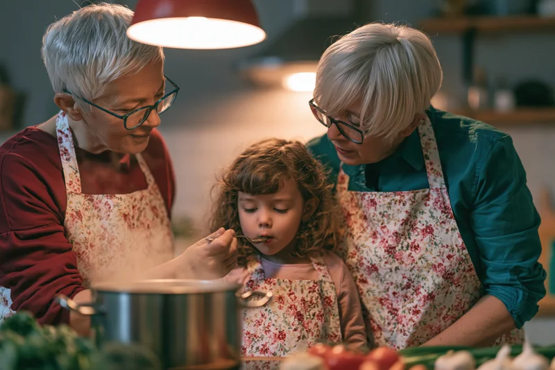 Grandmother and child cooking together in kitchen with spoon and vegetables