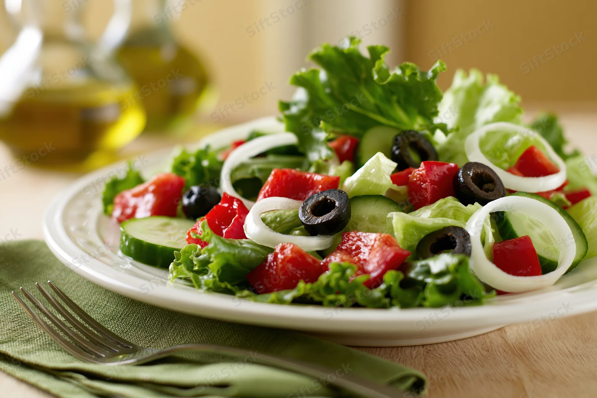 Greek-style salad with lettuce, tomato, cucumber, olives and onions on a white plate with fork and napkin on wooden table