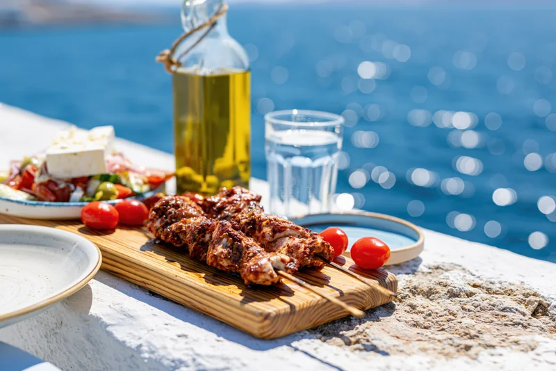 Grilled meat skewers and greek salad on a stone terrace by the ocean