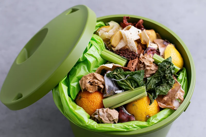 Green compost bin with open lid overflowing with fruit and vegetable scraps on countertop