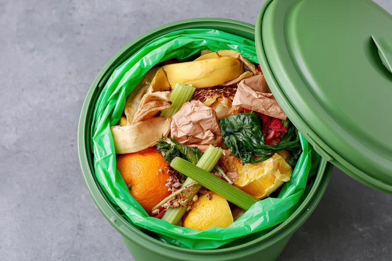 Open green compost bin filled with food scraps and organic waste on gray surface