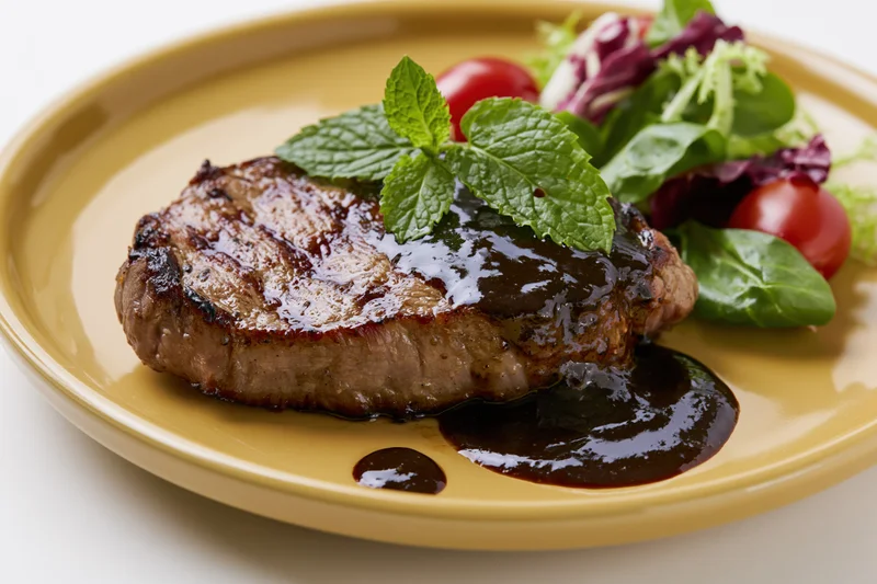 Grilled beef steak with black pepper sauce and fresh mint garnish on a yellow plate