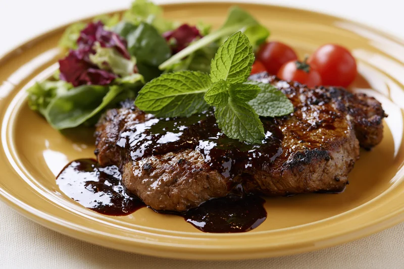 Grilled beef steak with black pepper sauce and mint garnish on a yellow plate with side salad
