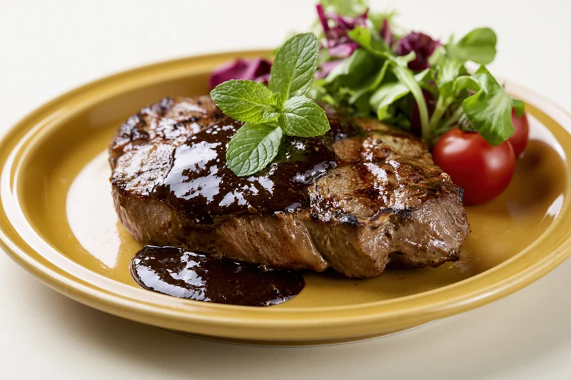 Grilled beef steak with black pepper sauce and fresh mint garnish on a yellow plate