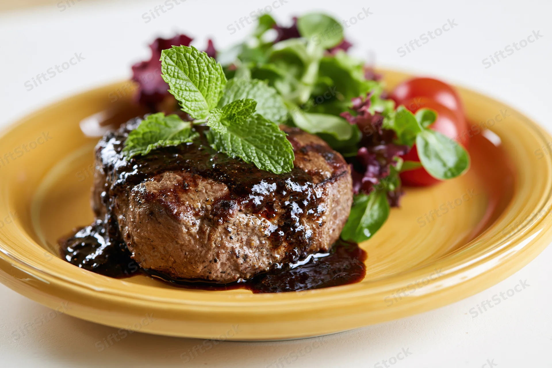 Grilled beef steak with black pepper sauce and mint garnish on a yellow plate