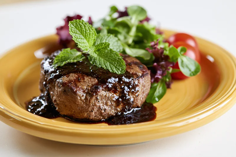 Grilled beef steak with black pepper sauce and mint garnish on a yellow plate