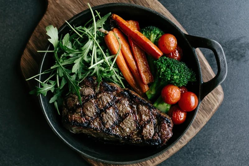 Grilled beef steak with vegetables in a cast iron skillet on a wooden board