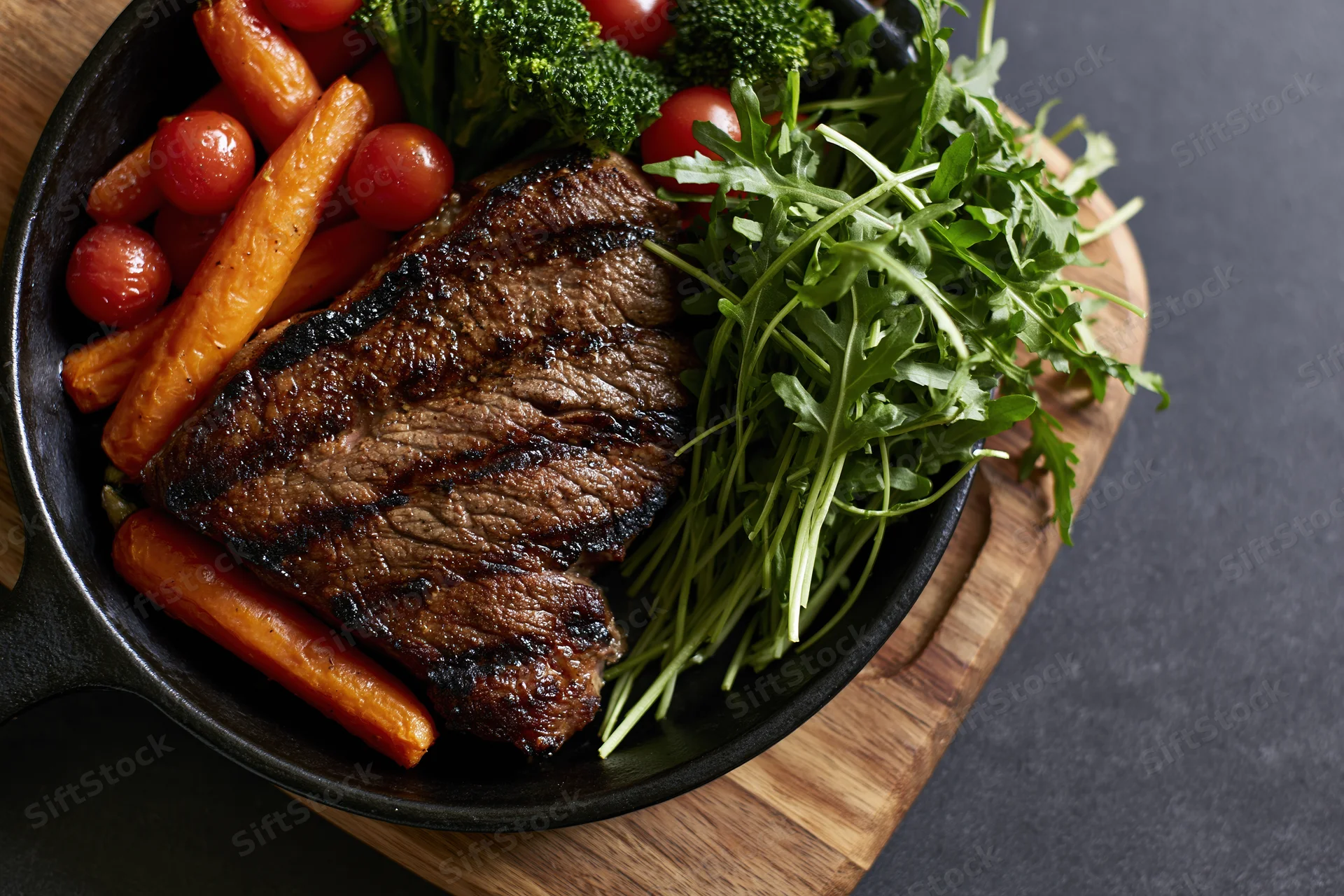 Grilled beef steak with vegetables in a cast iron skillet on a wooden board