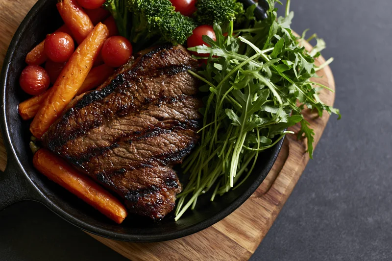 Grilled beef steak with vegetables in a cast iron skillet on a wooden board
