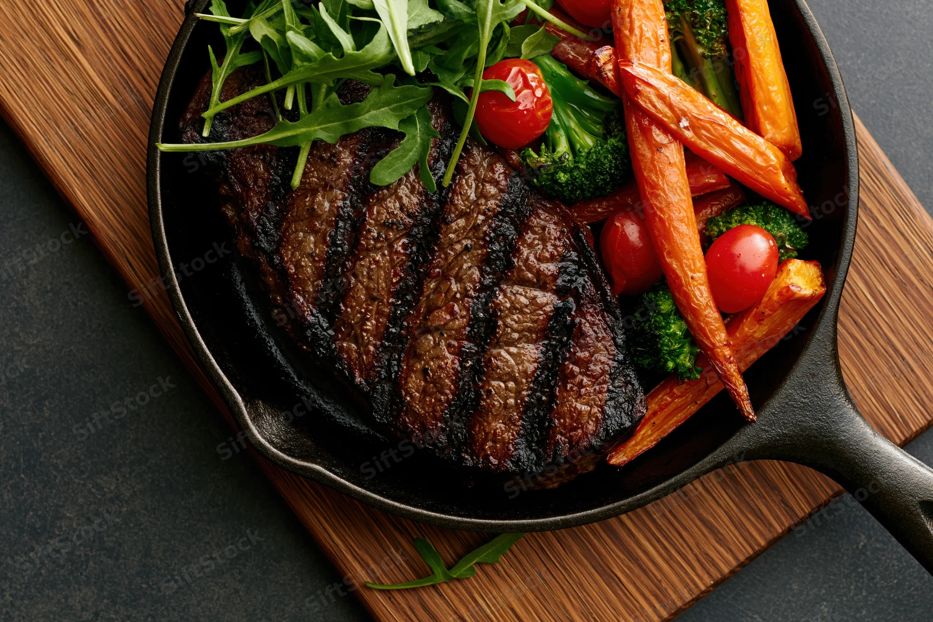 Grilled beef steak with vegetables in a cast iron skillet on a wooden board