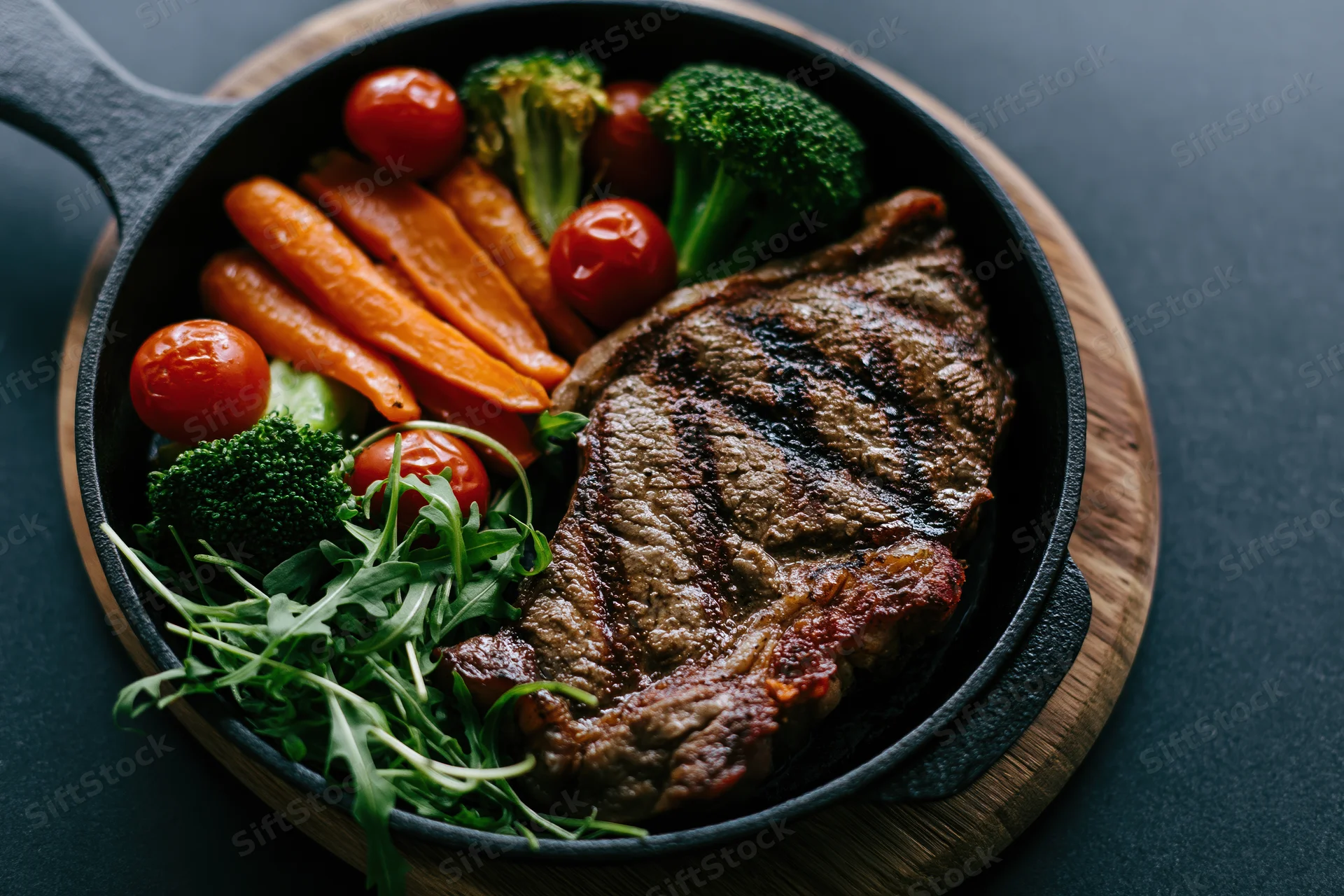 Grilled beef steak with vegetables in a cast iron skillet on a wooden board
