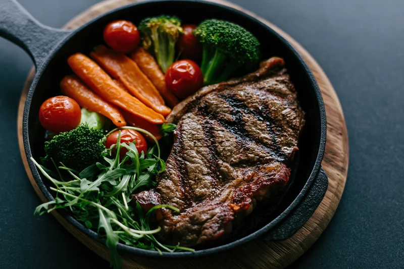 Grilled beef steak with vegetables in a cast iron skillet on a wooden board