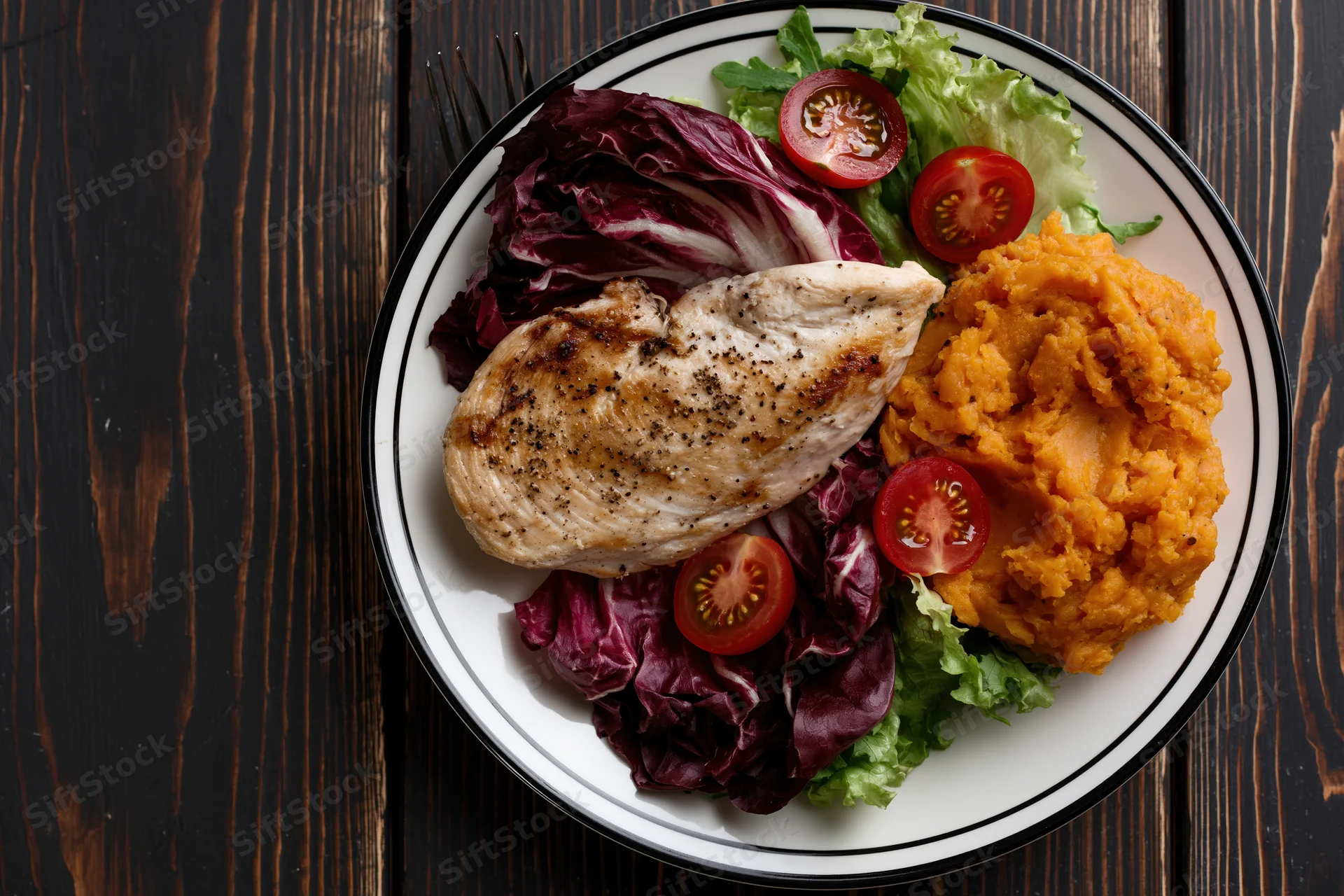 Grilled chicken breast with mashed sweet potato and mixed greens on a white plate on dark wooden table