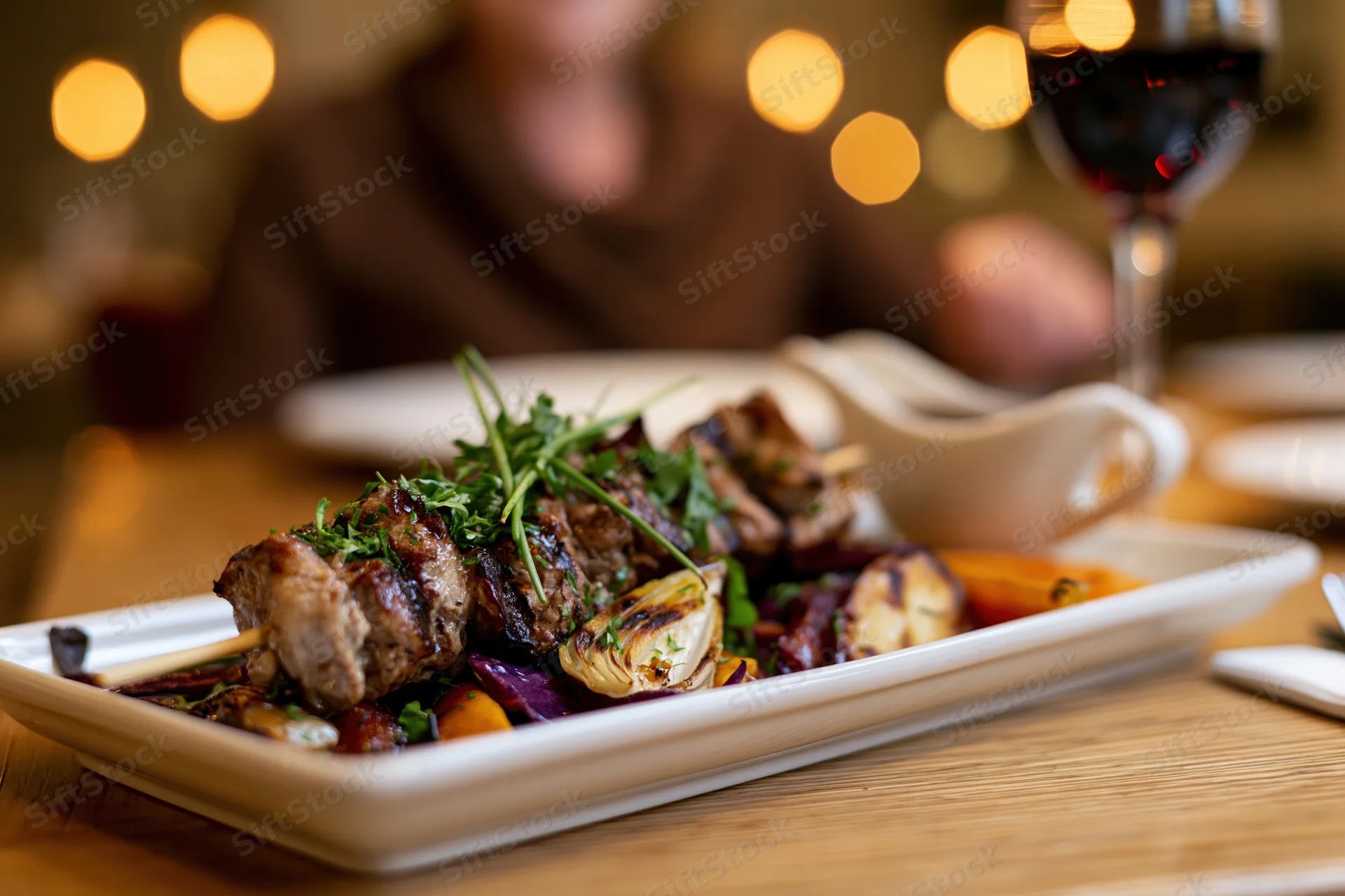 Grilled meat skewers with vegetables on a white ceramic plate at a restaurant table